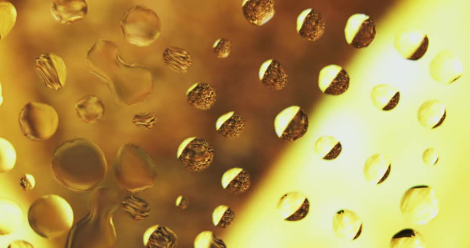 Water droplets sit on clear glass as yellow and amber light moves behind them