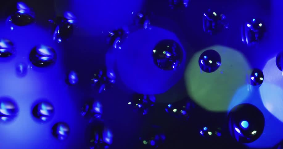 Circular colored lights move behind water droplets sitting on clear glass reflecting on the drops