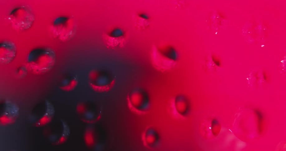 Colored lights shines on water droplets as they appear to turn and rotate as texture is reflected inside from the moving light