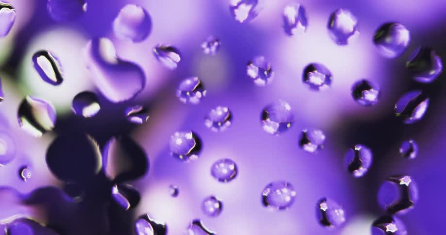 Colored lights shine on water droplets as they appear to turn and rotate as texture is reflected inside from the moving light