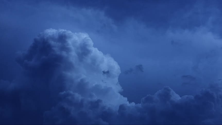 Cumulus clouds are floating in a dark sky as lighting flashes
