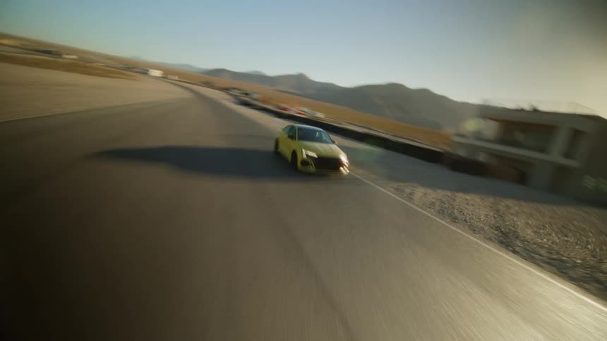 Dynamic aerial drone shot of a yellow sports car driving on a road through the desert at sunset