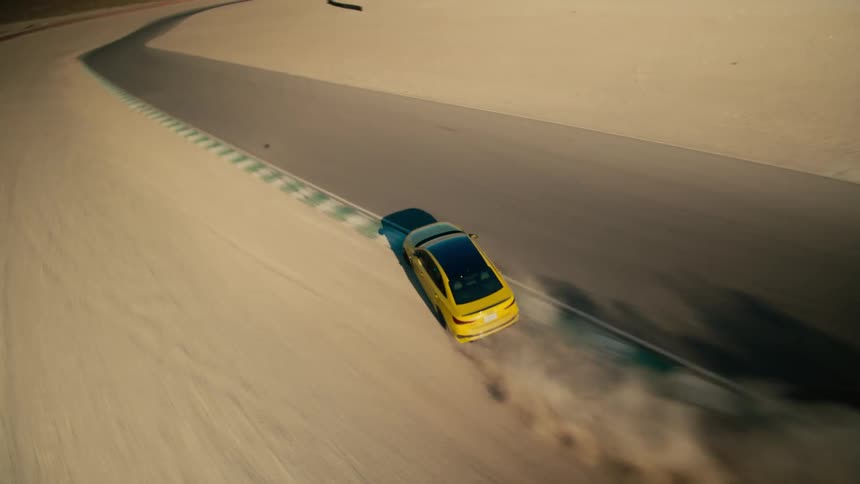 Aerial tracking of yellow sports car going fast on closed course in the desert during the day while straddling the shoulder intermittently