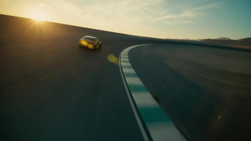 A yellow automobile slides as it speeds around a curve on a desert road with mountains in the distance