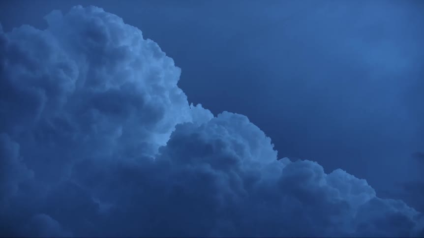 Cumulus clouds are moving across a dark blue sky