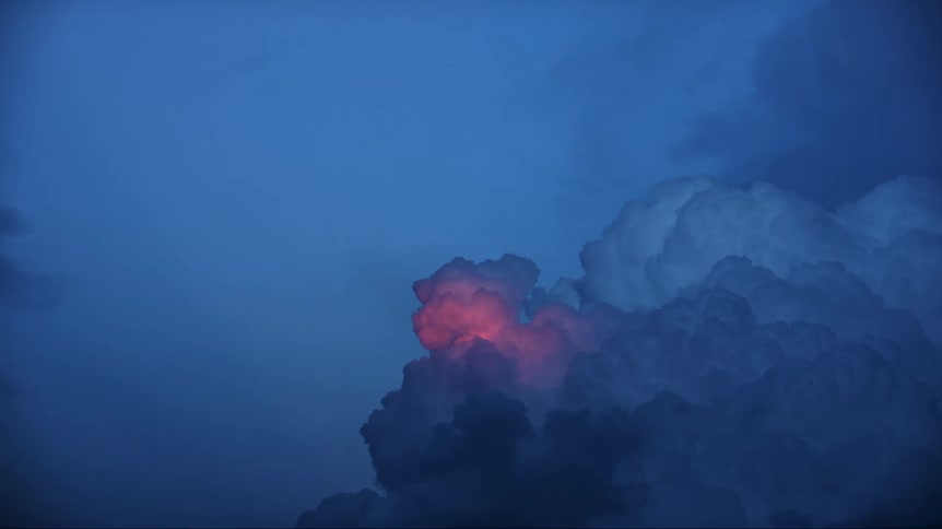 Sunlight shines on cumulus clouds creating a pink area as dark storm clouds move across the sky