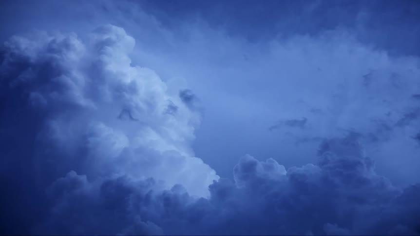 Cumulus clouds are floating in a dark sky as lighting flashes