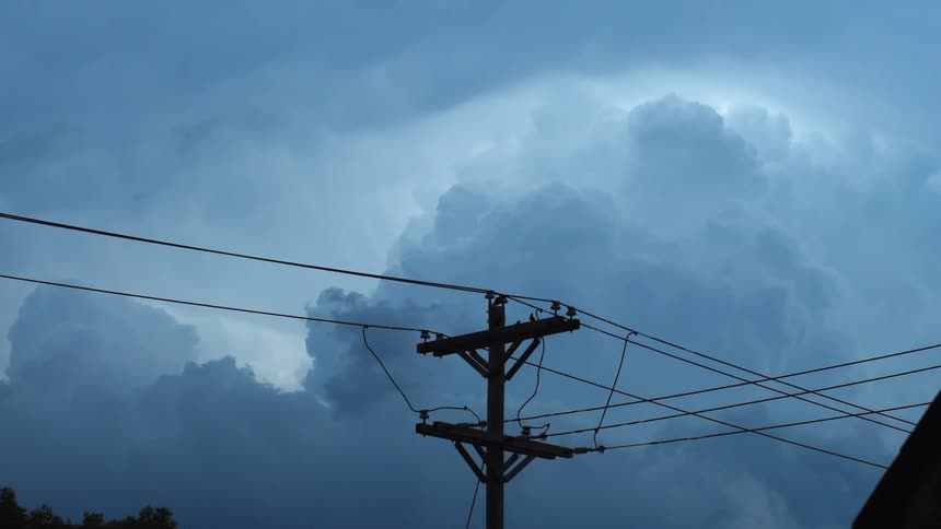 Cables run across a utility pole where a bird is perched looking around as storm clouds move across the sky
