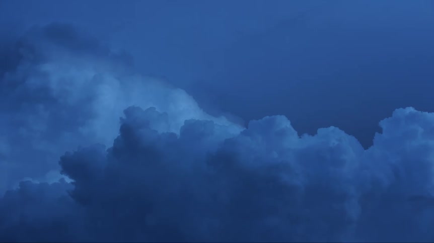 Cumulus clouds move across a darkening azure blue sky