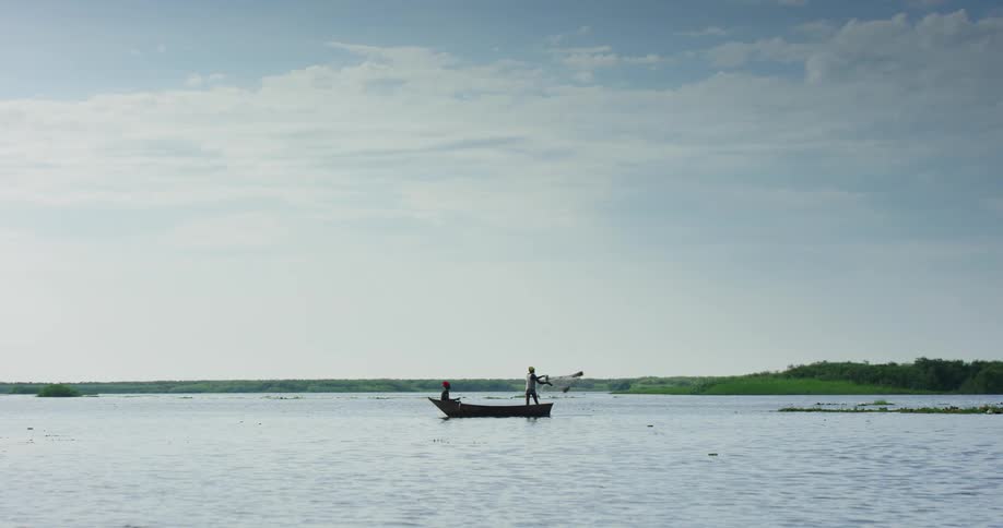 One person paddles boat while the other throws a fishing net