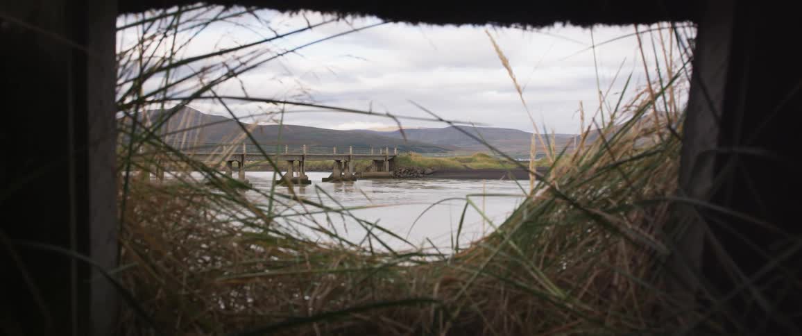 Structure opening allows view of bridge over river with mountains on the horizon