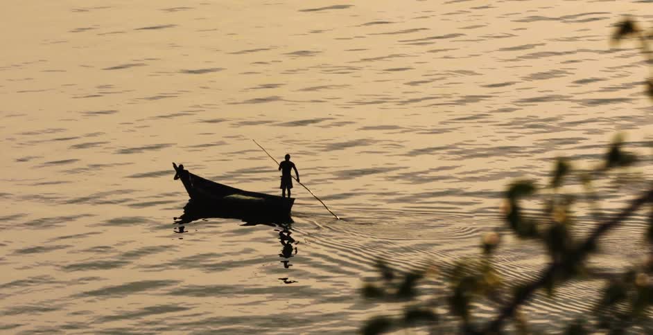 A silhouette of a person paddling a boat while standing