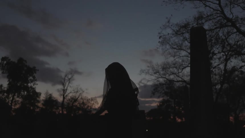 A woman adjusts her veil while standing outside at dusk