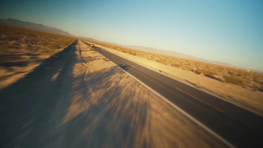 Dynamic aerial drone shot of a yellow sports car driving on a road through the desert at sunset