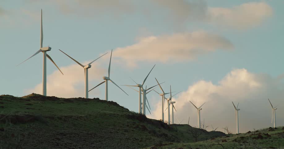 Wind turbines are lined up across the top of a hill on a windfarm under a cloudy sky