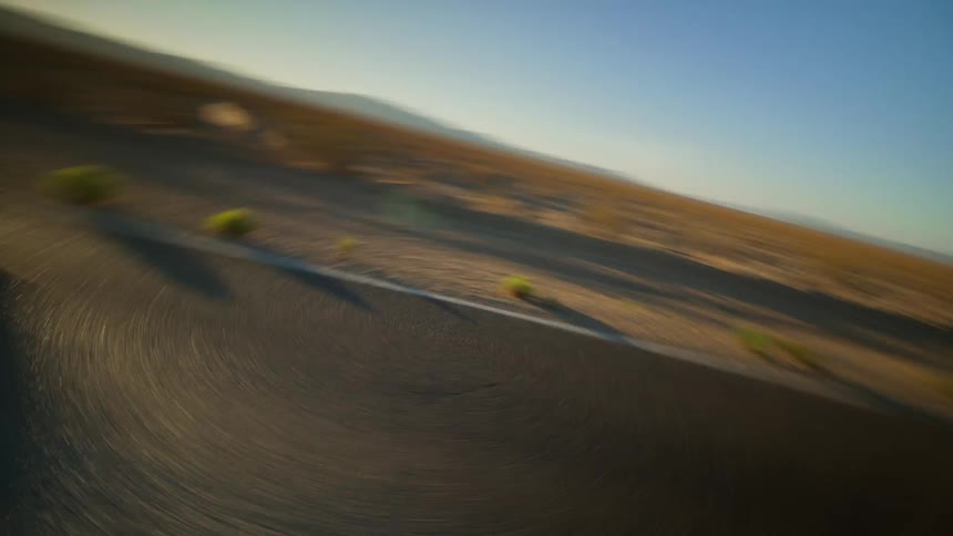Car speeds along highway past scrub land on a sunny day