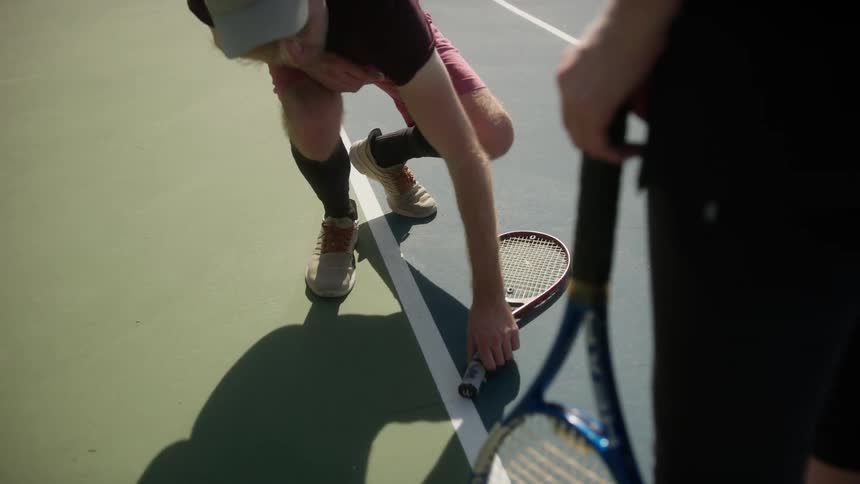 Two people standing near each other as one person bends over to pick up a tennis racket