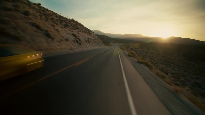 A car travels along a road through a vast countryside during the day