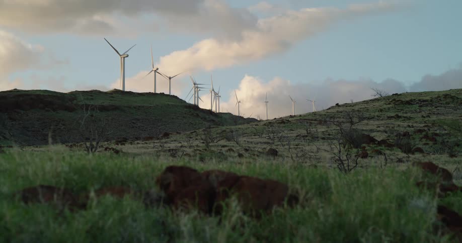Wind turbines are lined up across the top of a hill on a windfarm under a cloudy sky