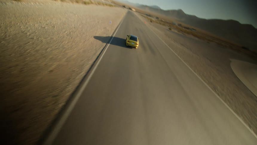 A car speeds down a road through the desert during the day