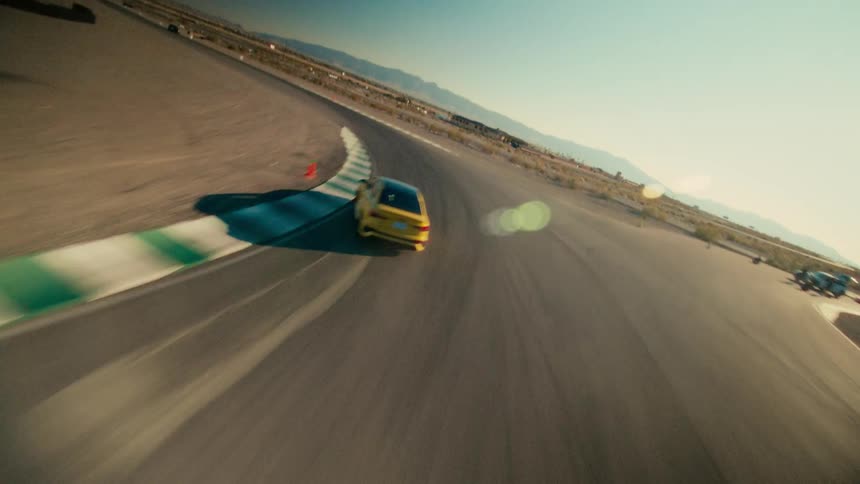 Sports car speeds along race track with mountains in the distance