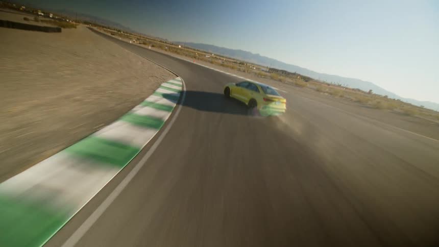 A car drifts while cornering on a race track in an arid countryside during the day