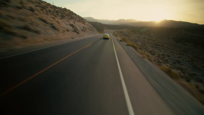 Sportscar drives along highway through scrub land as sun peaks over mountain