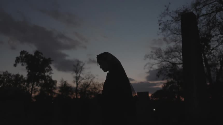 Woman stands mourning in a cemetery at dusk