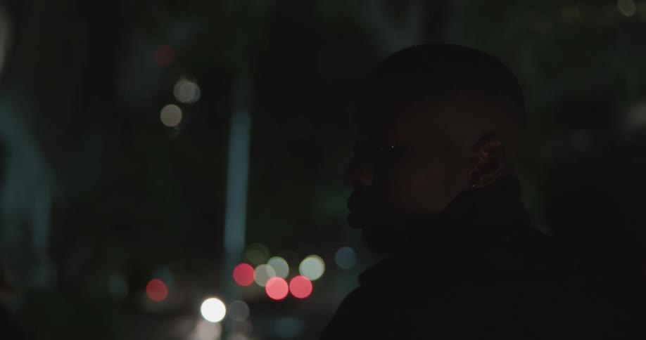 Man walking with women through city at night turns as headlight shines across them