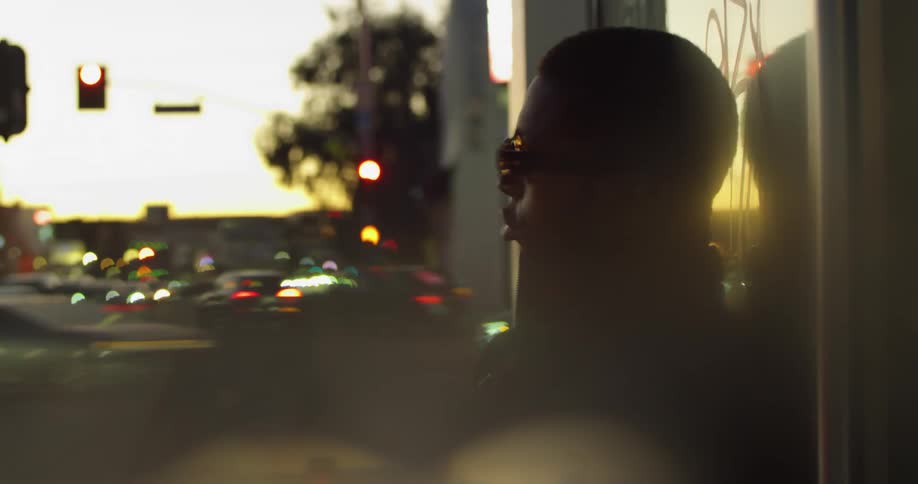 An up close of a mans face while he stands against a building at dusk with sunglasses on