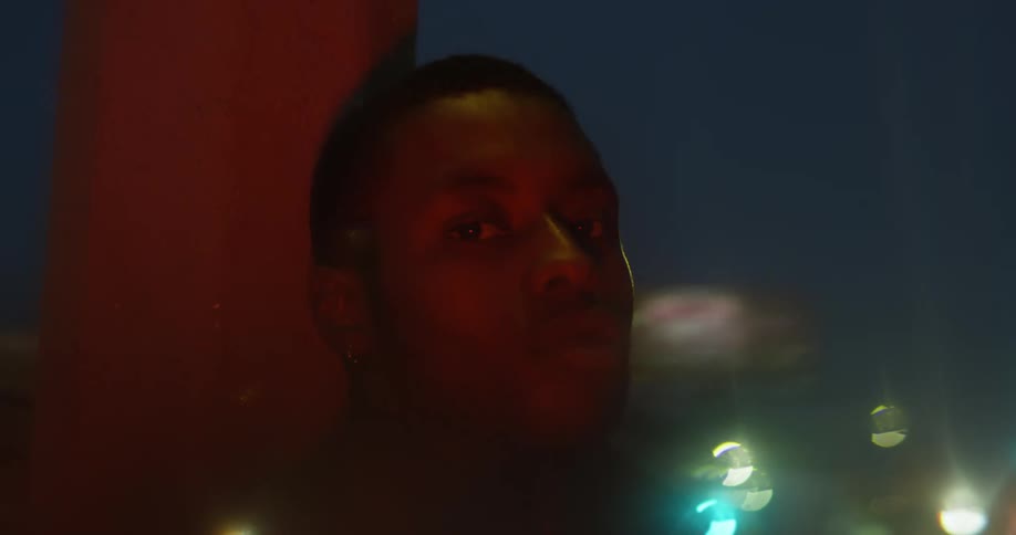 Man leans against pole at night with the blurry lights of the citybehind him