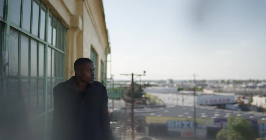 Man in black coat leans agains balcony railings and looking at the view
