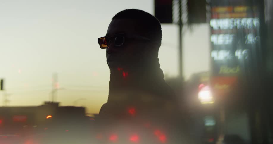 Man stands looking at busy road as afterglow tints sky