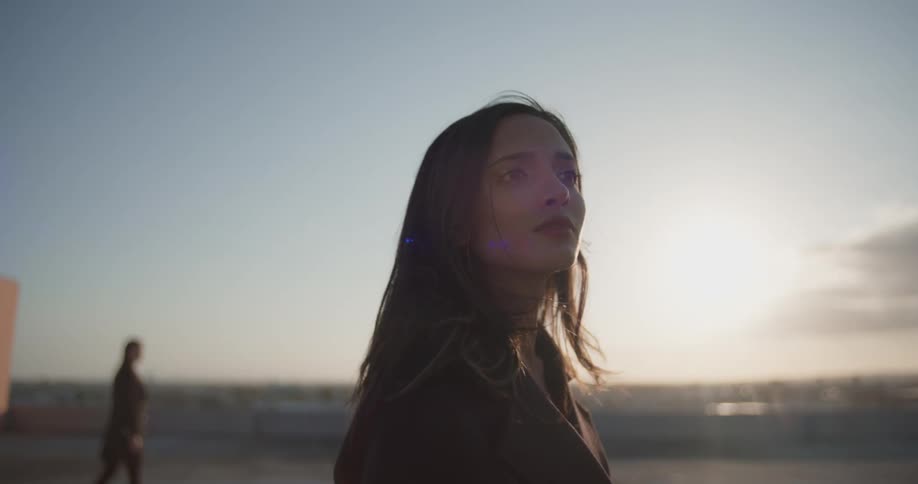 A woman looking off into the distance contemplatively with two people walking around behind her