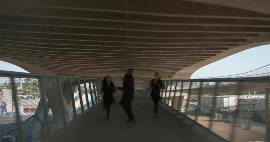 Three people dance around on a pedestrian bridge downtown