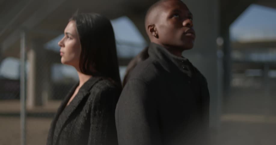 Three models wearing gray coats pose near base of underpass