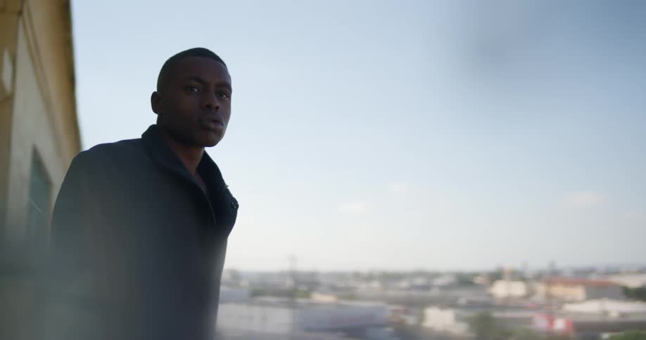 Man with black overcoat looks around on balcony
