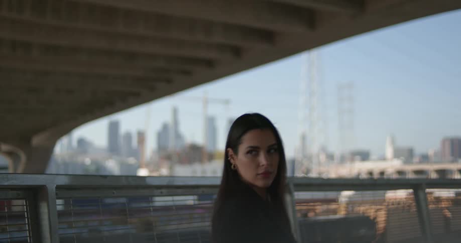 Woman exchanges glance with man walking the opposite direction under an overpass then she walks backwards briefly