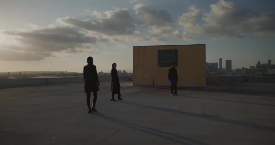 Three people walking around slowly on top of a building with a large city in the background