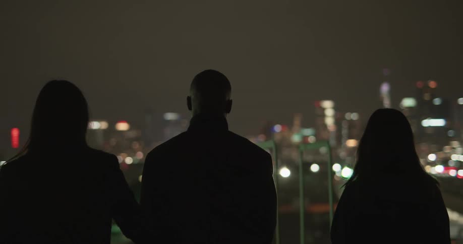 Three peoples silhouettes standing looking over a lit up city at night