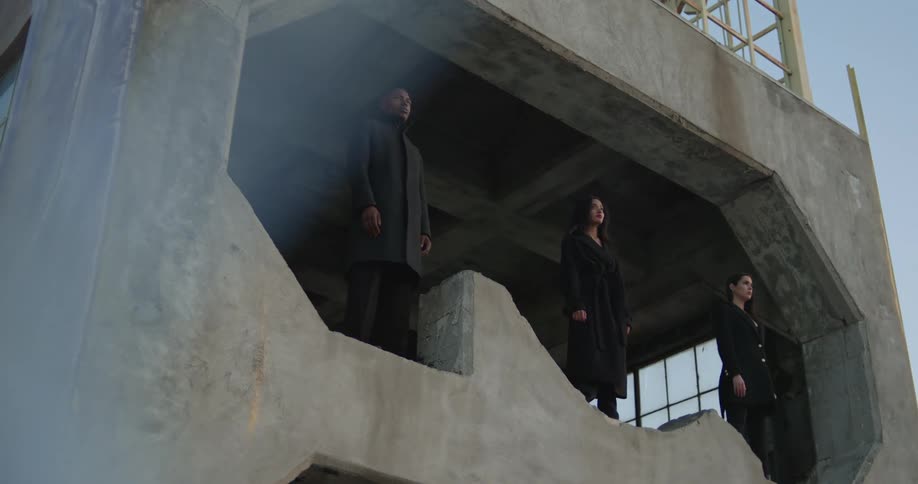 Two women and a man stand on some kind of structure with a shape carved into it that they are standing in