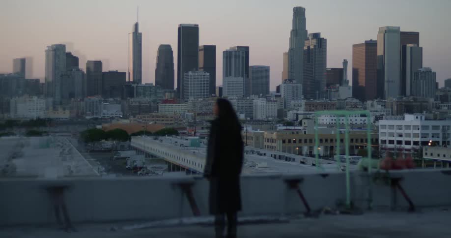 Woman stands near half wall looking toward downtown skyscrapers