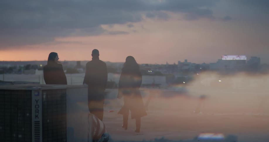 Three people walk past an air conditioning unit on a buildings rooftop