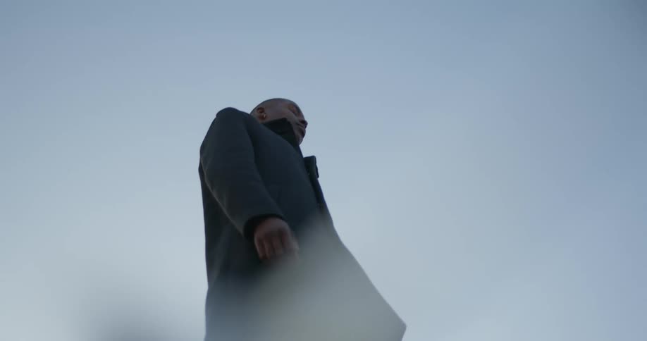 Man wearing long coat stands outdoors under a blue sky