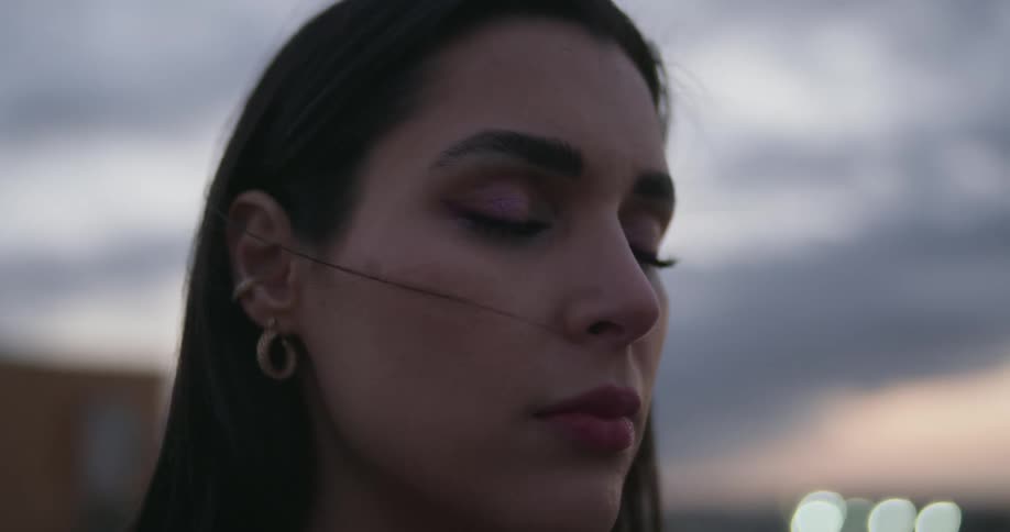 Woman stands outdoors with her eyes closed