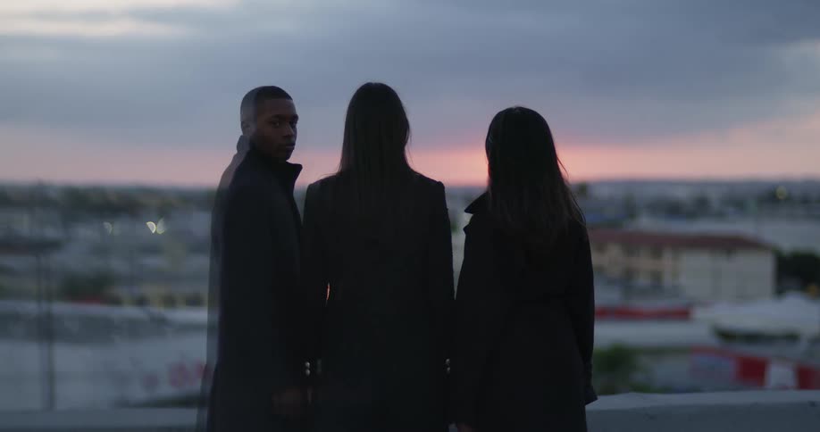 A man turns around while standing on a building rooftop with two women