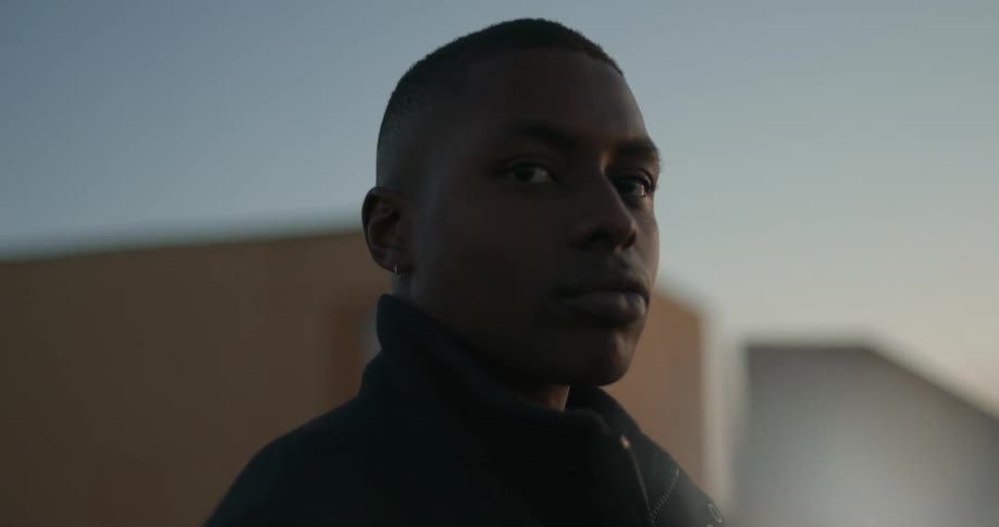 A man is standidng outside with his eyes focused in a certain area and there are buildings in the distance