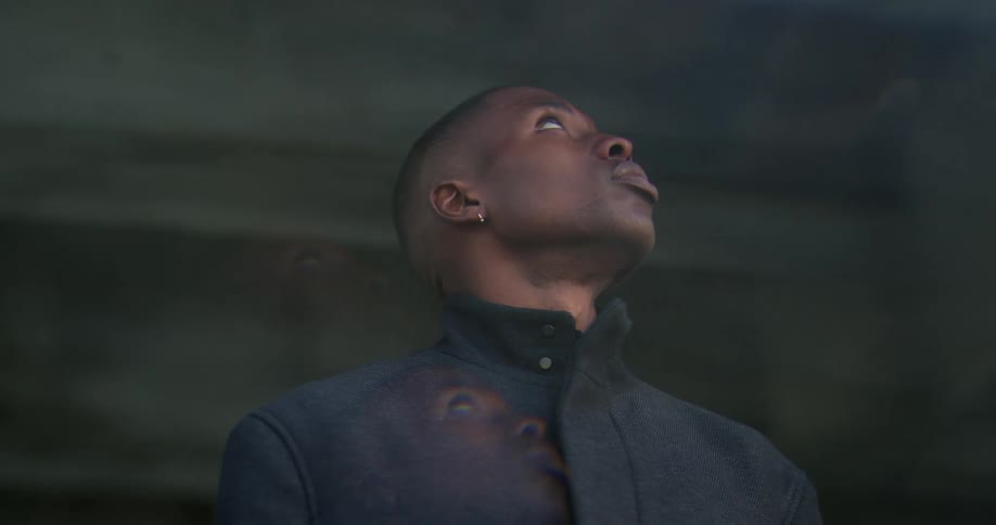 A man stands outside and looks up as if hes following something with his eyes all the way down