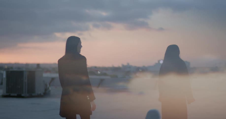 Women with black hair black coat and blazer jacket walk down on top of building at dusk