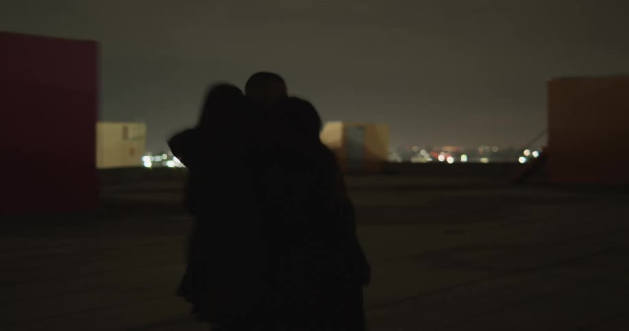 Three people walking two woman and a man with lights flashing behind them